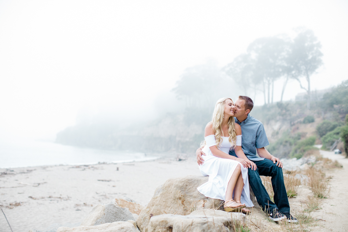 california foggy beach with couple snuggling on the rocks