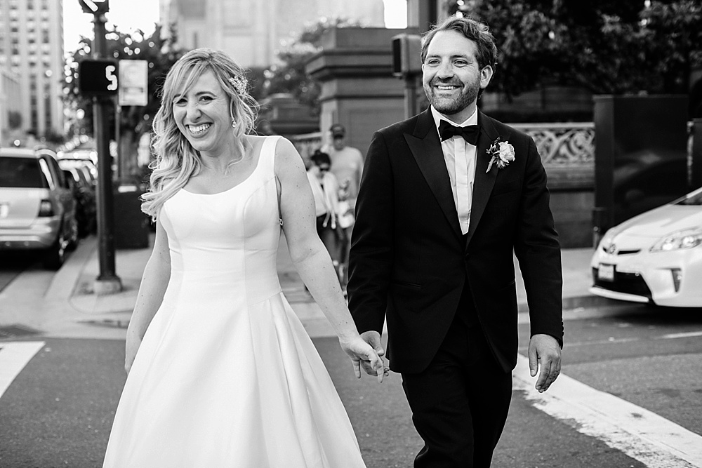 Bride and groom smile as they cross the street at the fairmont san francisco wedding by amy thompson photography
