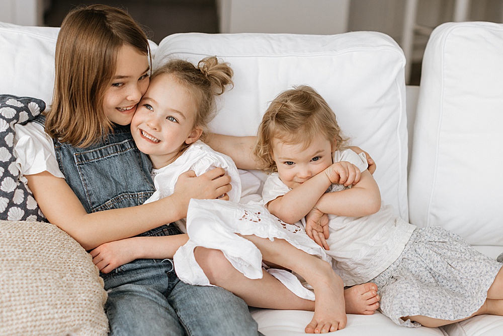 three sisters cuddled on the couch for family photo shoot at home by amy thompson photography